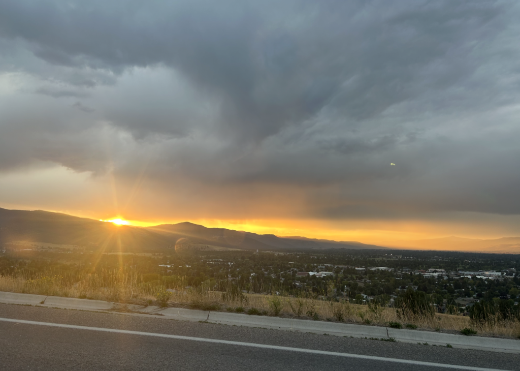 The sun peaks out from overcast clouds to set behind a stretch of mountains.